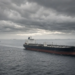 Oil tankers on a dark, overcast sea, conveying Hormuz shipping-risk escalation without battle-damage stills or invented map coordinates.