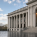 Classical U.S. finance facade on a wet plaza with a descending yield-curve glow in the arched window, as the 10-year retreats from a near-5% spike.