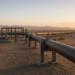 A desert crude pipeline on steel supports beside an idle valve station at first light.