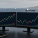 Oil trading desk with rising futures charts overlooking tankers at sea, as Brent and WTI push higher on Middle East chokepoint pressure.