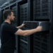 A technician slides a 2U server chassis into a data-center rack, illustrating an AI-server hardware surge.