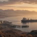 Tanker beside a coastal energy terminal under desert mountains at golden hour, illustrating southern Saudi energy and Red Sea export-route risk.