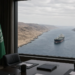 US and Saudi flags at a conference table, a tanker in a narrow desert strait through the window.