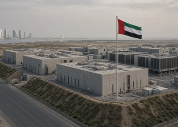 Dispersed concrete data halls behind a UAE flag, Abu Dhabi towers on the horizon.