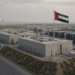 Dispersed concrete data halls behind a UAE flag, Abu Dhabi towers on the horizon.