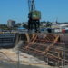 Naval shipyard dry dock with large steel hull and cranes, conveying shipbuilding acquisition competition.