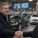 Handshake inside a vehicle auction hall with cars and bidding screens, illustrating Copart's cash deal to buy ACV Auctions.