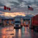 Freight trucks at a Canada–United States border crossing under mountain dusk light, symbolizing cross-border commerce and tariff tension.