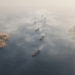 Aerial view of tankers in a hazy narrow strait between arid coasts, conveying Hormuz transit-flow uncertainty and residual crude risk premium.
