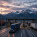 Freight trucks at a Canada-United States border crossing under mountain dusk, symbolizing cross-border trade and tariff tension.